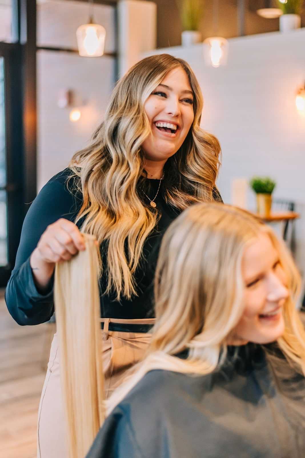 Woman smiling, holding long hair of client at a salon.